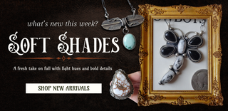 Promotional banner for 'SOFT SHADES' jewelry featuring multiple silver-toned necklaces and pendants with black, white, and turquoise elements, alongside a hand holding a carved stone pendant. The layout includes text reading 'what's new this week?', 'SOFT SHADES', 'SHOP NEW ARRIVALS', and a gold-framed display containing more jewelry.